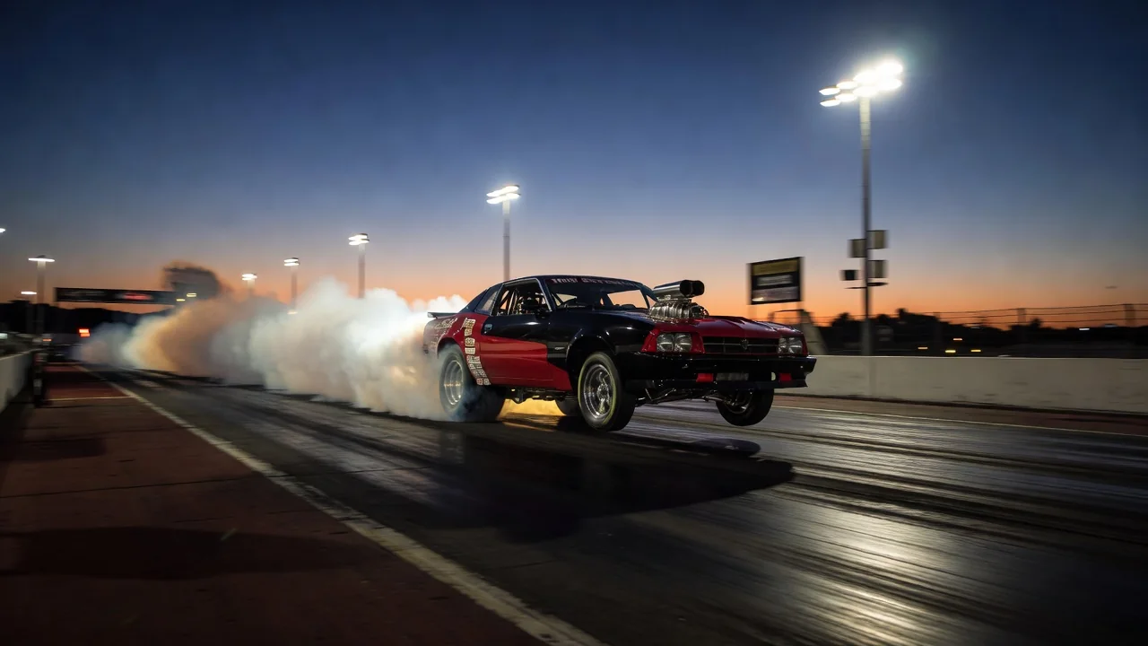 A door-slammer drag car launching off the starting line at a drag strip at dusk